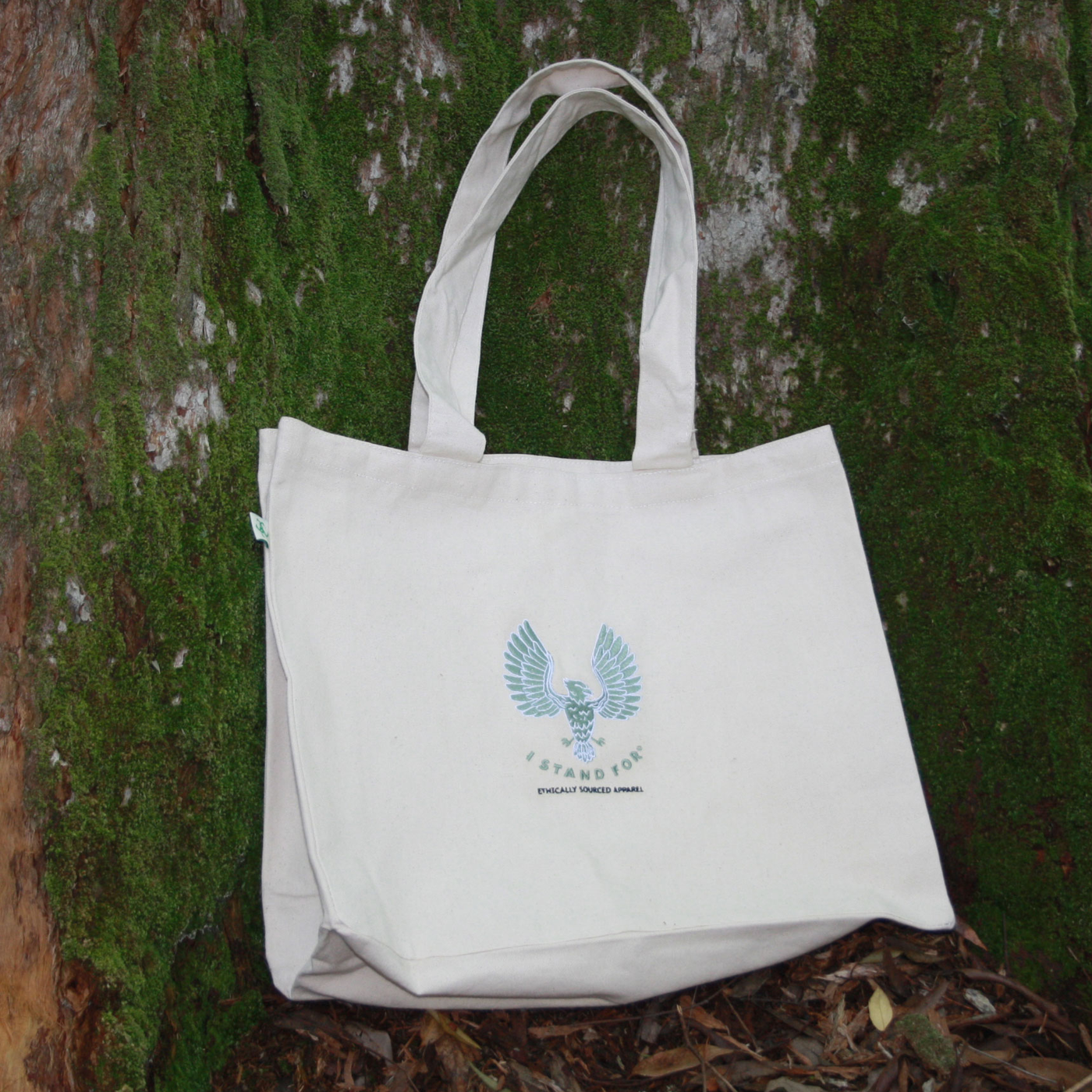 Organic canvas tote bag rested against a tree features two internal pockets