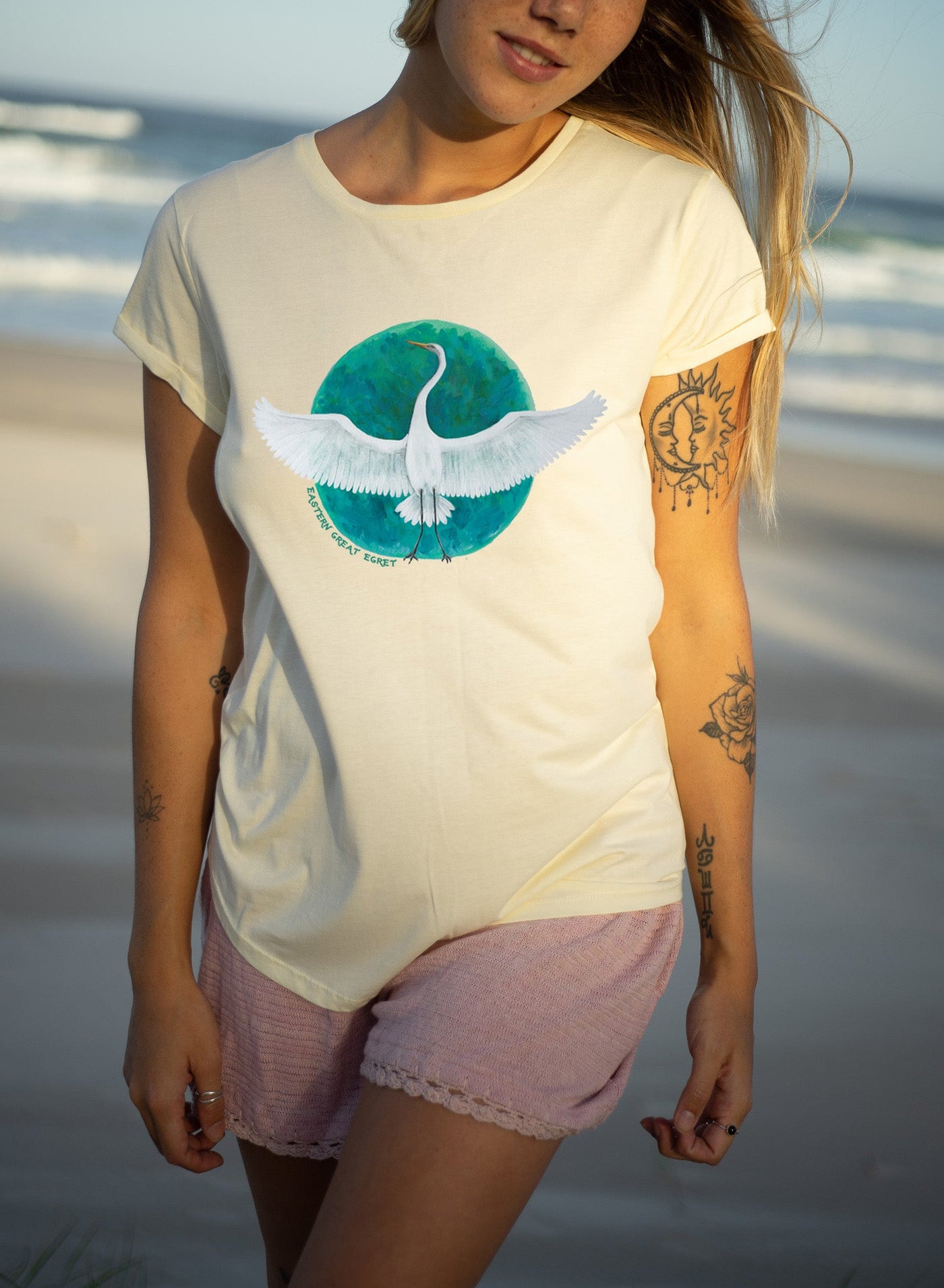 Pale yellow rolled sleeve t-shirt. White bird graphic across chest on top of green earth shape.